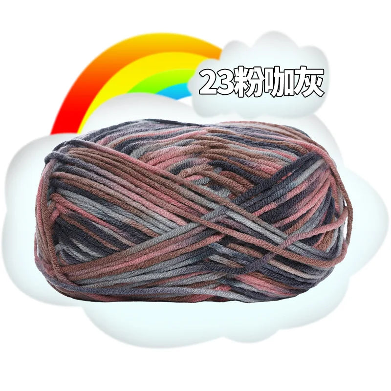 A ball of dark gray and pink milk cotton blend yarn is shown against a white cloud with a rainbow background.