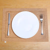 A white dinner plate and silverware are placed on a tan linen placemat on a wooden table.