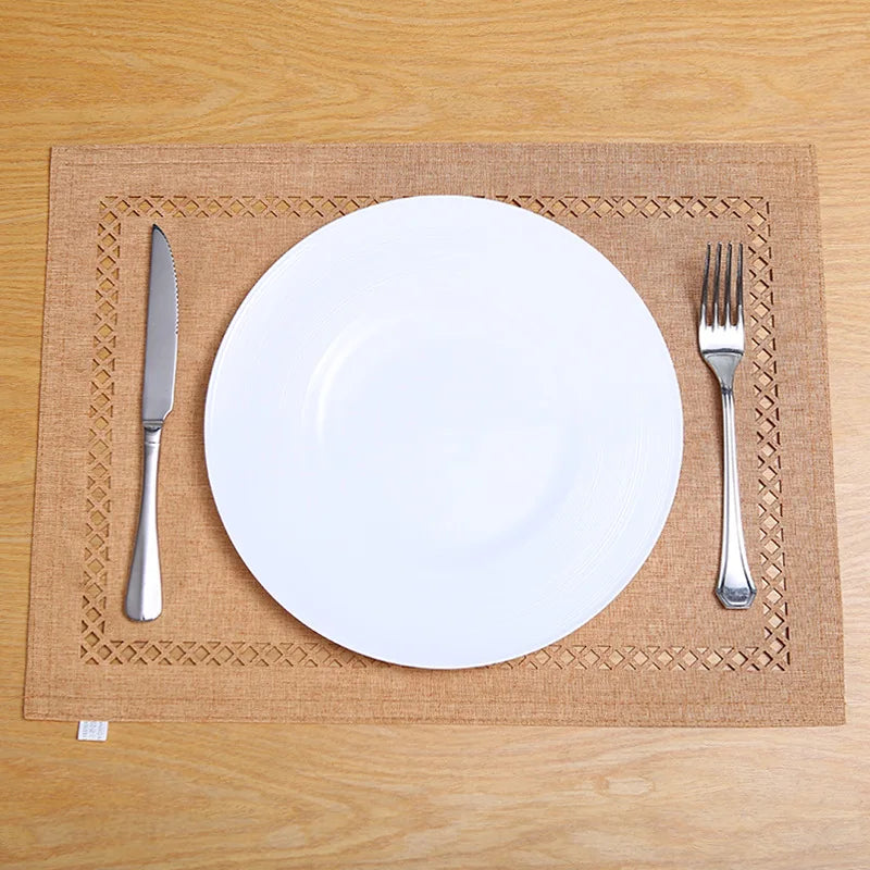 A white dinner plate and silverware are placed on a tan linen placemat on a wooden table.