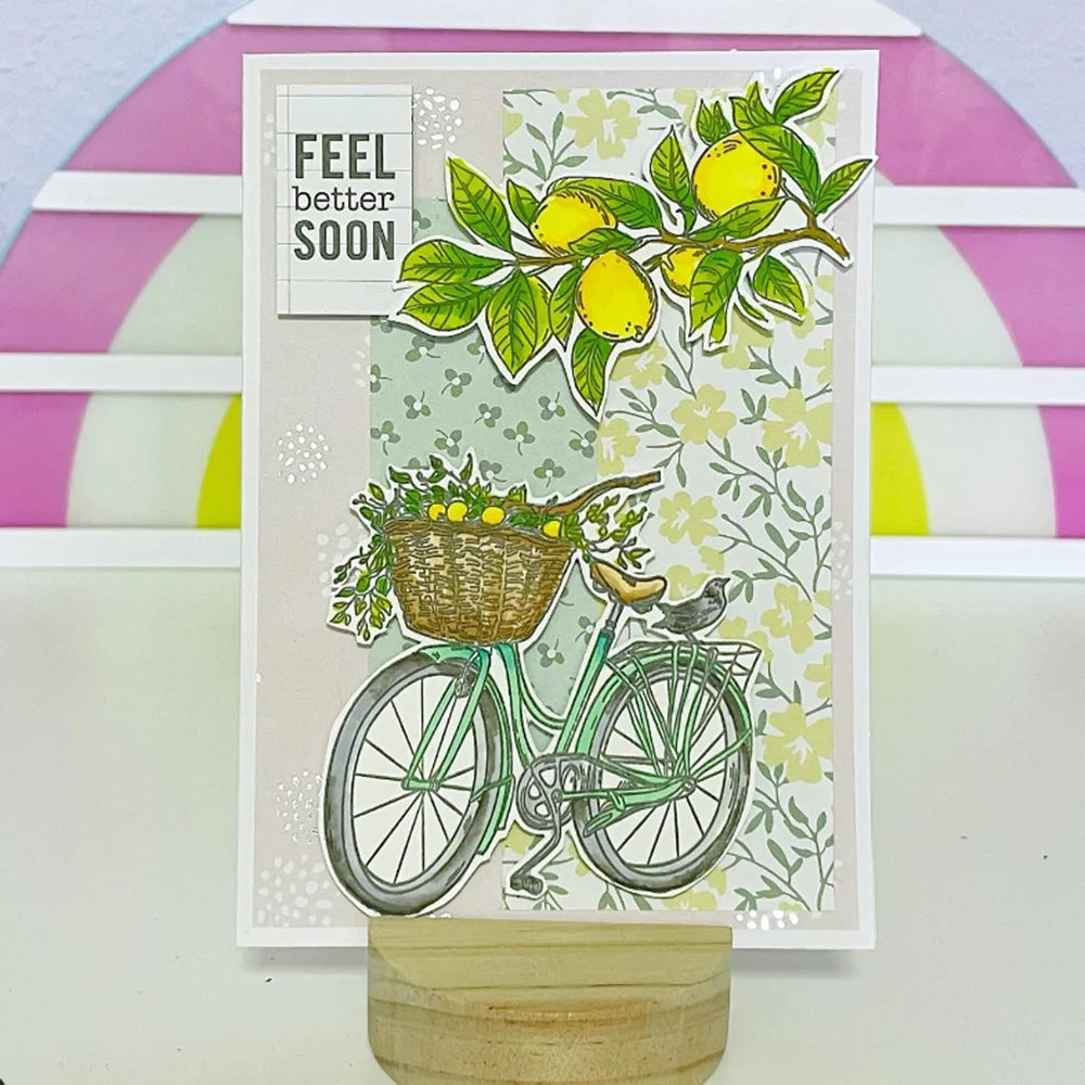 A die and stamp set featuring a green bicycle, yellow lemons, and greenery on a light patterned card.