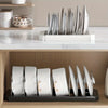 A white organizer rack holds multiple silver-colored expandable pots and pans on a wooden shelf.