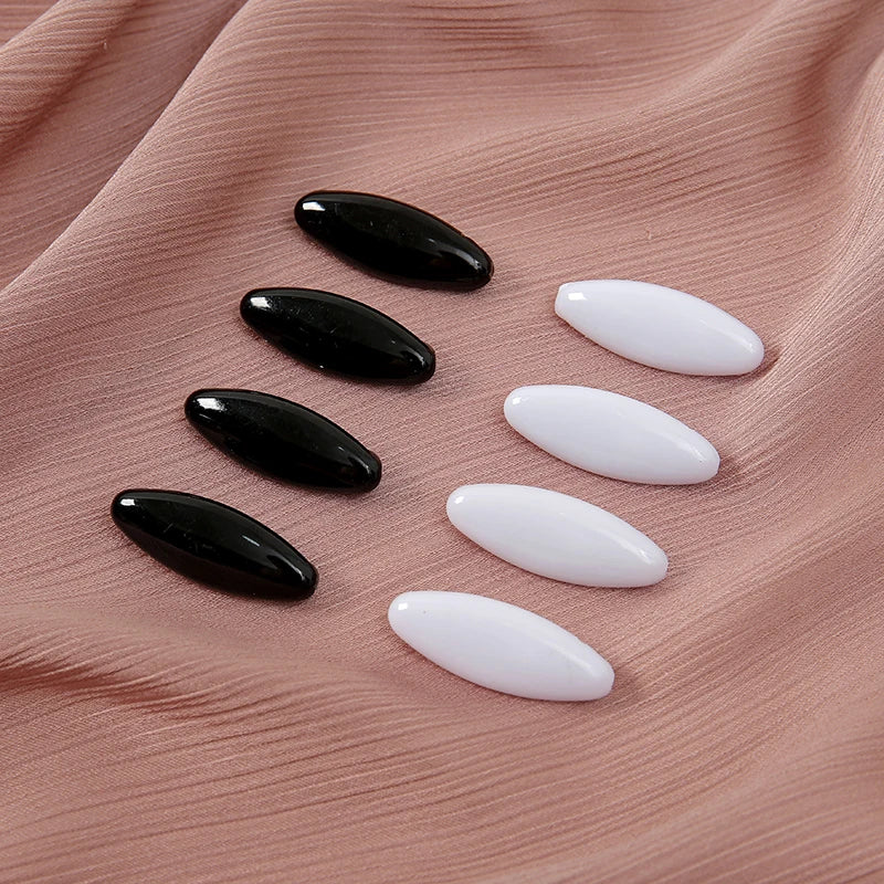 A set of eight solid color scarf pins in black and white are displayed on a pink fabric.