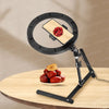 A black foldable overhead tripod with a ring light is positioned above a bowl of red berries on a wooden table.