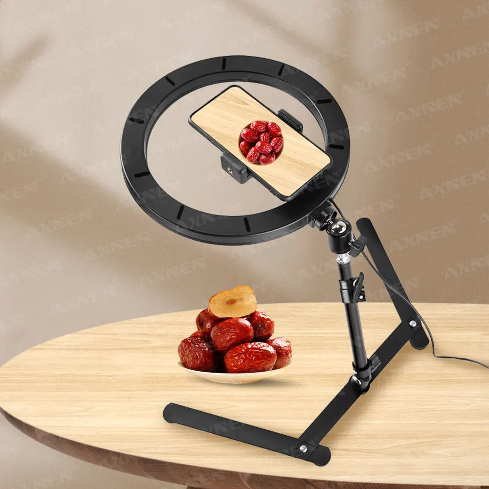 A black foldable overhead tripod with a ring light is positioned above a bowl of red berries on a wooden table.