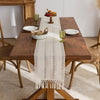 Beige boho table runner with tassels on a wooden table set for a meal.