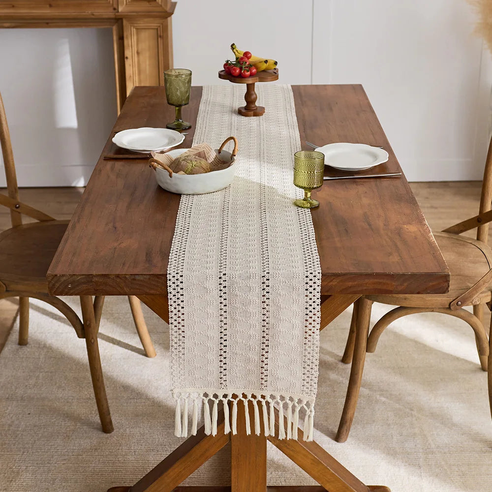 Beige boho table runner with tassels on a wooden table set for a meal.