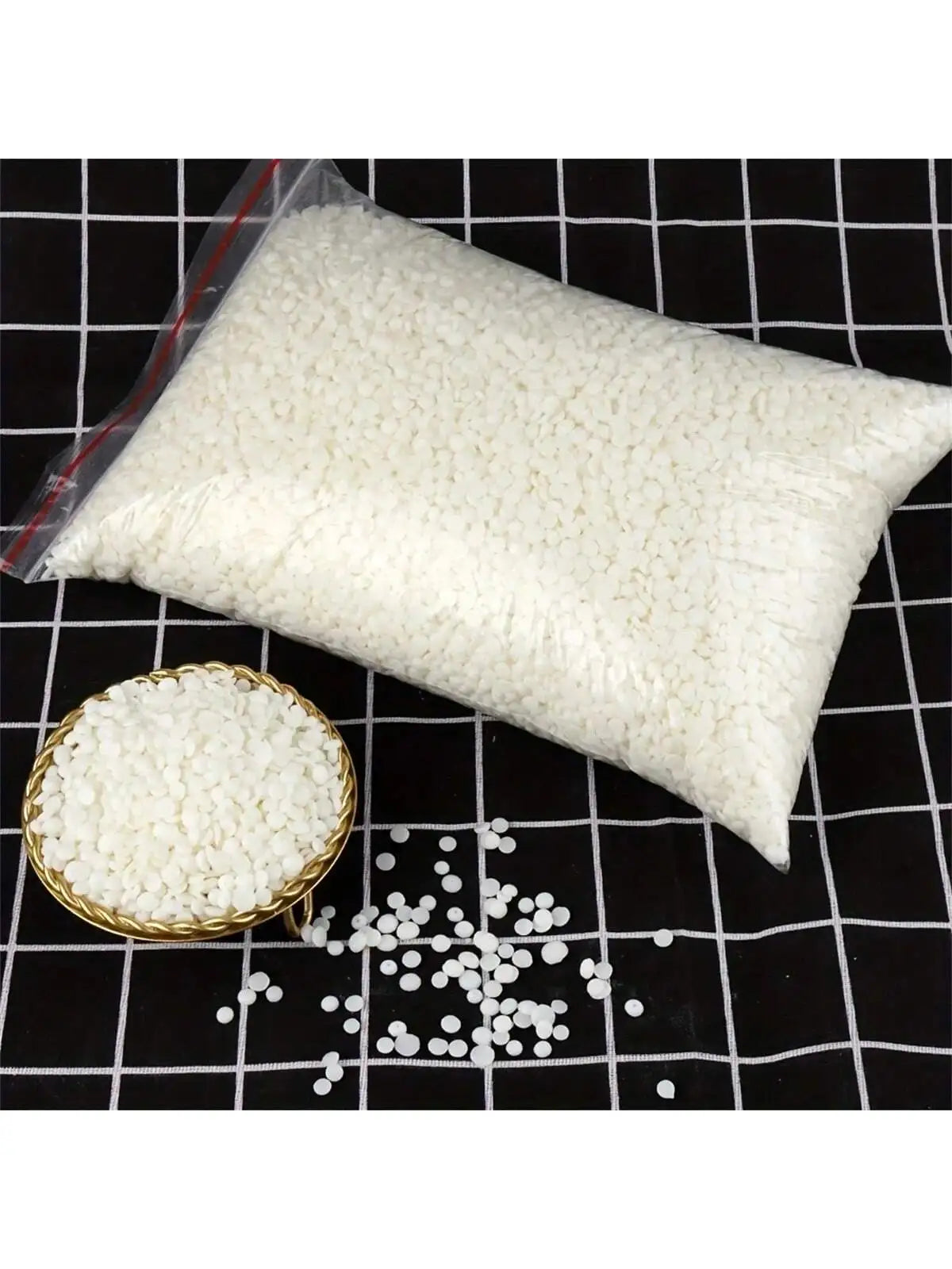 A white bag of natural soy wax granules next to a small bowl of the same granular material on a black grid surface.