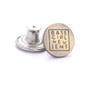 A round brass button with the text BASE GIRL NEW JENS engraved on it, next to a silver button base.