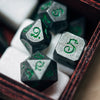 A close-up view of seven metal polyhedral dice with a dragon font set inside a dark red box.