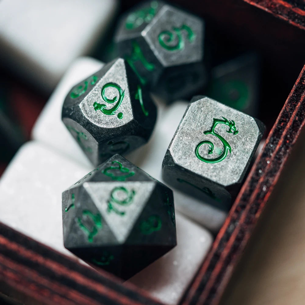 A close-up view of seven metal polyhedral dice with a dragon font set inside a dark red box.