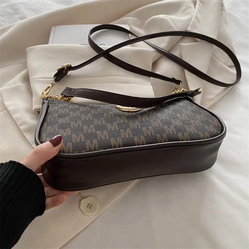 A dark brown PU leather crossbody bag with a gold accent chain is shown resting on a white fabric background.