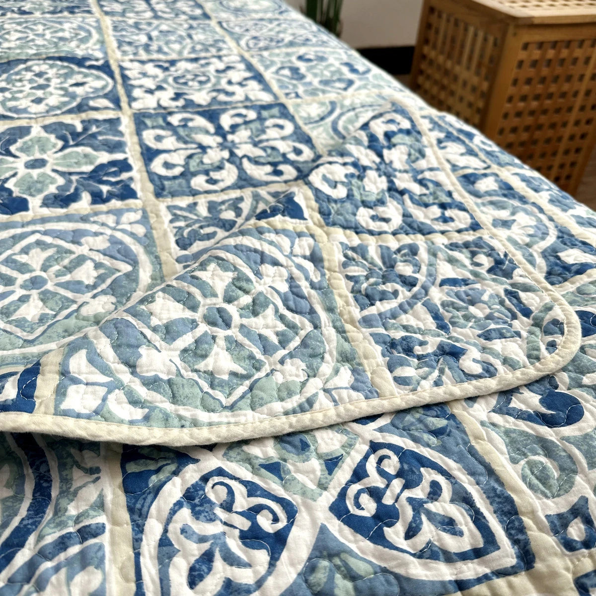 A blue and white patchwork cotton bedspread with a quilted pattern is displayed on a surface.