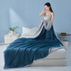 A teal cooling summer quilt draped over a white bed, with a model wearing a light top standing beside it.