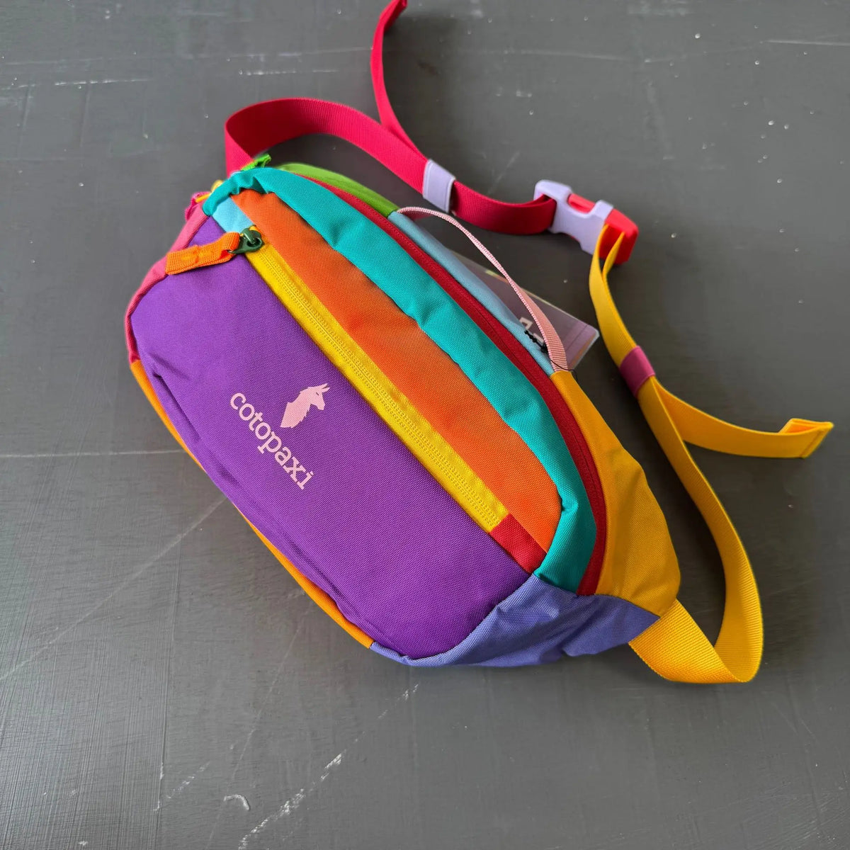 A colorful, striped nylon fanny pack featuring purple, yellow, green, and blue blocks, with a pink strap.