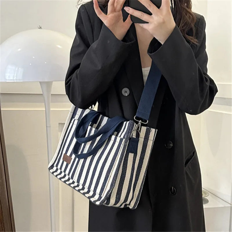 A person holds a striped canvas tote bag with inner pockets against a light background.