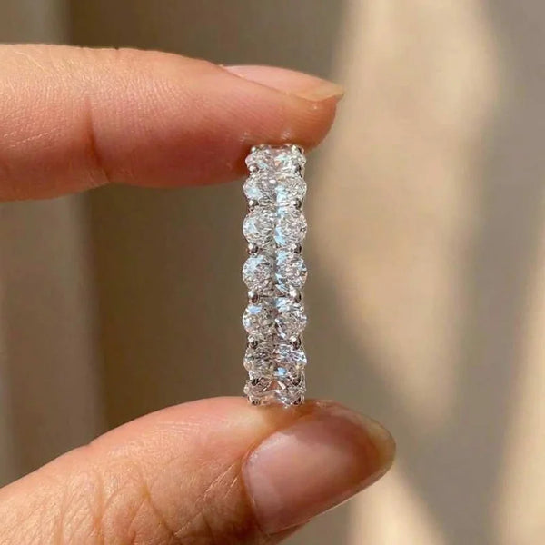 A hand holds an oval cubic zirconia sterling silver ring with a pave setting of small stones.