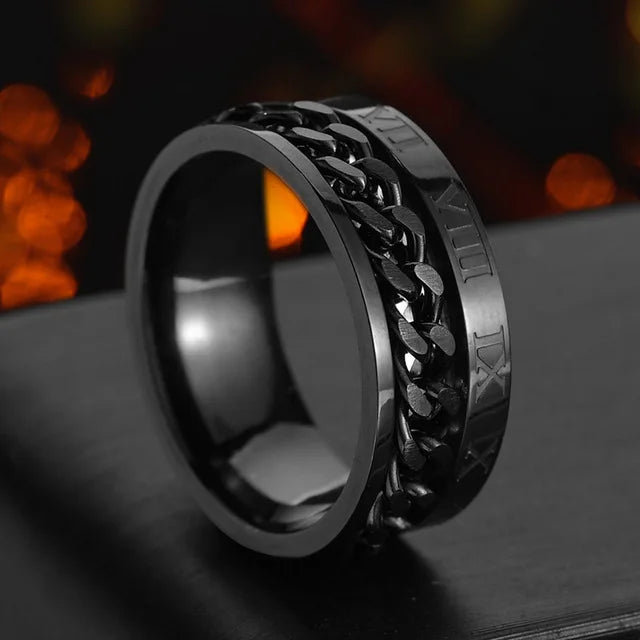 A close-up shot of a black stainless steel spinner ring resting on a dark surface.