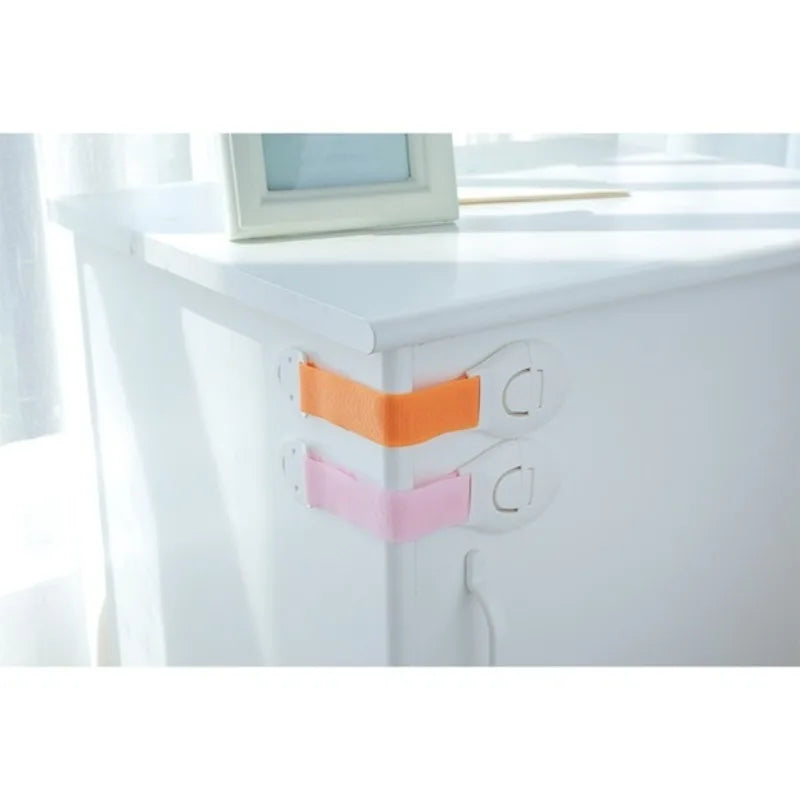 Close-up of white cabinet doors showing orange and pink adhesive baby proofing latches.