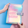 A hand holds a shiny pink envelope organizer for a 100 envelope savings challenge against a blue and pink background.