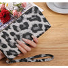 A hand holds a black and white leopard print retro long wallet on a wooden table.