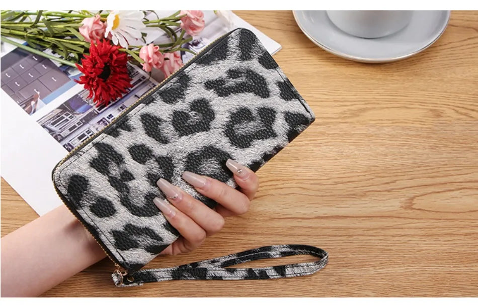 A hand holds a black and white leopard print retro long wallet on a wooden table.