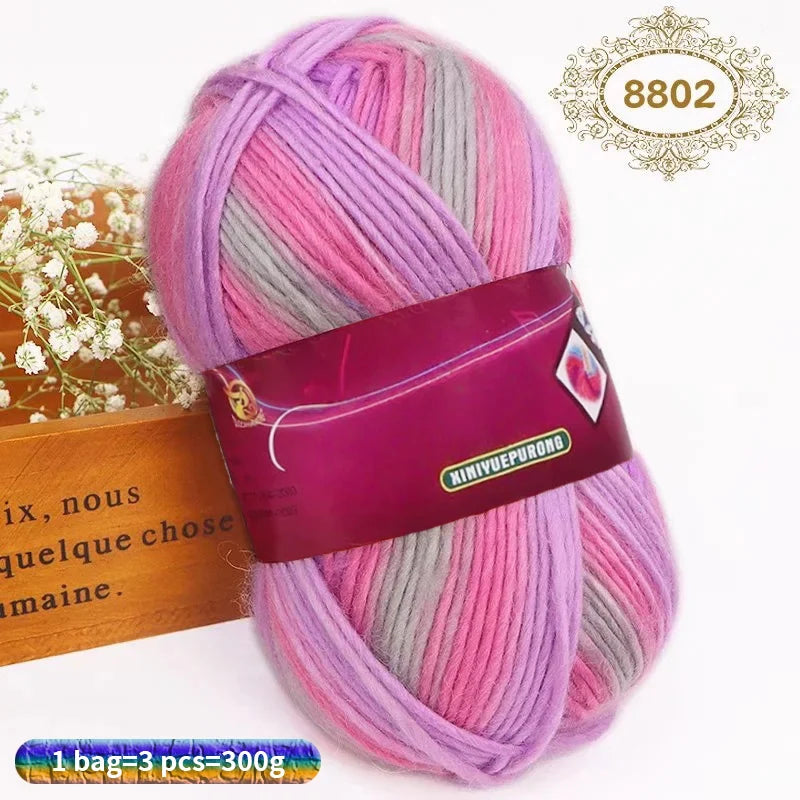 A skein of gradient pink and gray wool blend yarn is shown next to a wooden box.