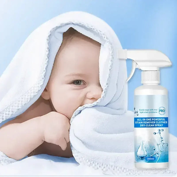 Un bébé est enveloppé dans une serviette blanche à côté d'un flacon pulvérisateur de détachant tout-en-un pour vêtements.