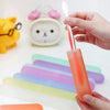 A hand holds an orange travel toothbrush case with a white brush inside, next to colorful silicone toothbrush holders.
