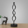 A black and white, twisted seaweed-shaped desk lamp with a dark base.