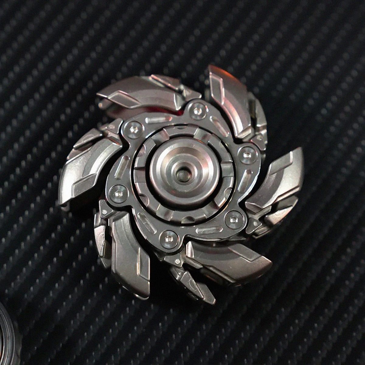 A metallic, multi-bladed fidget spinner with a silver finish resting on a dark textured surface.