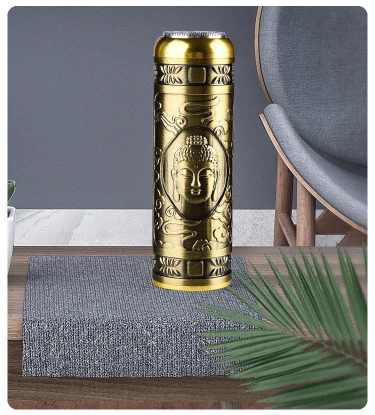 A gold-colored, cylindrical electric razor with a Buddha face design rests on a gray textured mat on a wooden surface.