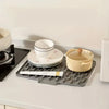 A silicone dish drying mat with quick drainage is shown on a white countertop next to ceramic dishes and a yellow bowl.