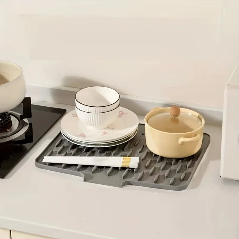 A silicone dish drying mat with quick drainage is shown on a white countertop next to ceramic dishes and a yellow bowl.