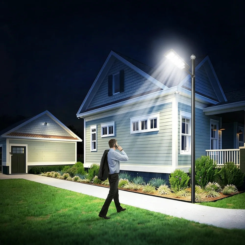 A person stands outside a house at night, looking up at a bright solar street light illuminating the front of the building.