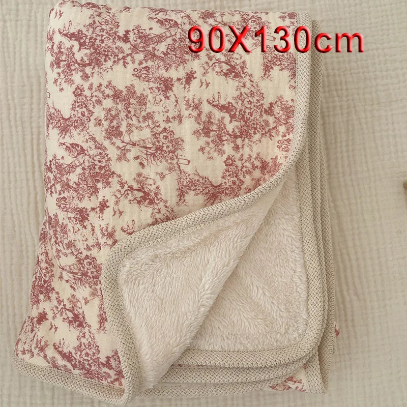 A folded floral muslin baby blanket in beige and pink tones, showing a soft, textured fabric.