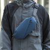 A man wearing a gray waterproof jacket with a blue running waist pack attached to his shoulder.