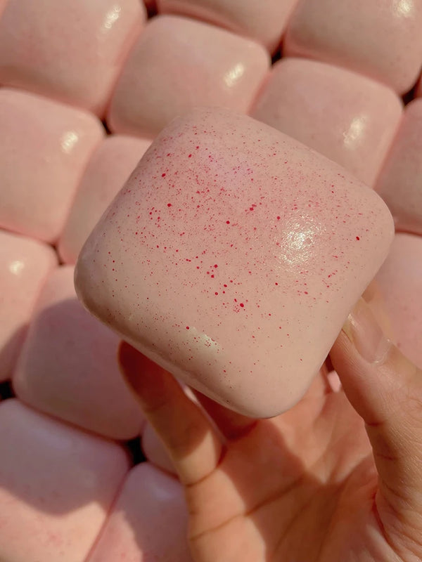 A pink squishy toast fidget toy with red speckles is held in a hand.