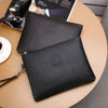 Schwarzes, elegantes Leder-Clutch-Portemonnaie für Herren auf einem Holztablett neben einer Zeitschrift.