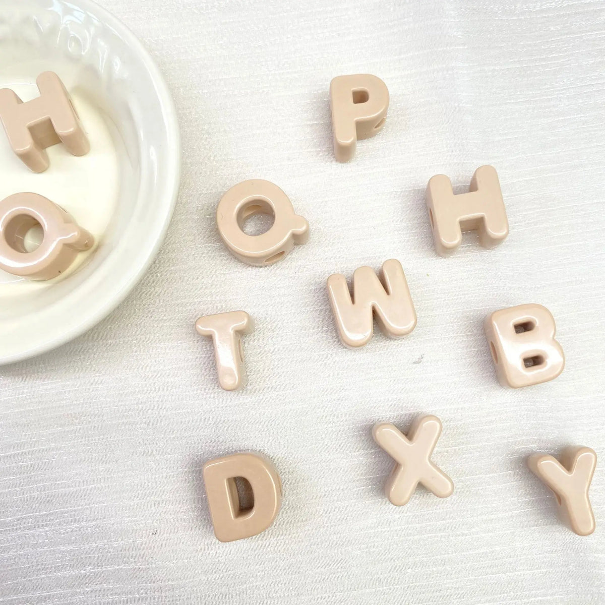 Collection de perles en acrylique de couleur beige clair formant les lettres H O P T W H B D X Y, éparpillées sur une surface