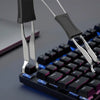 A close-up view of a black mechanical keyboard with a silver keycap puller being used to remove or adjust a keycap.