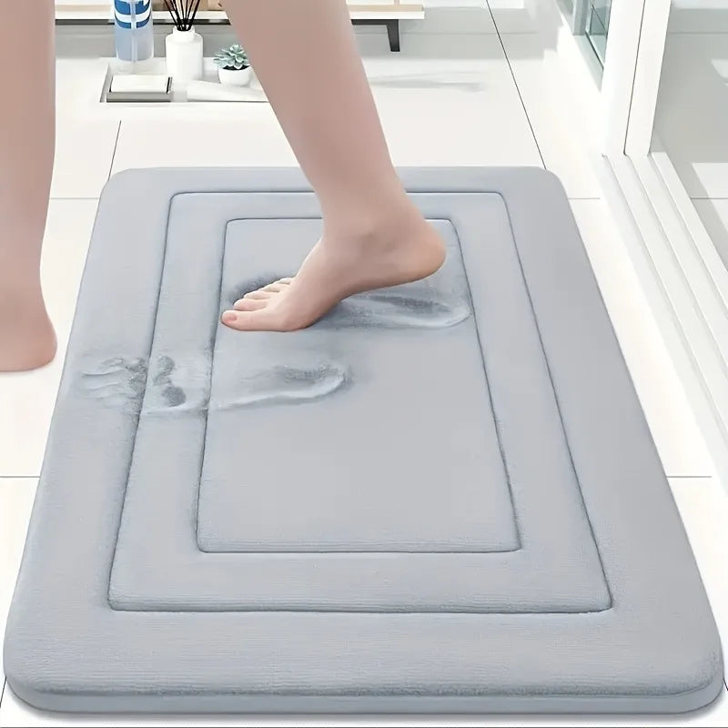A person's foot is placed on a gray absorbent soft non-slip bath mat for foot soaking or relaxation.