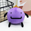 A cute purple plush doll with a yellow crown and black features sitting on a white surface.