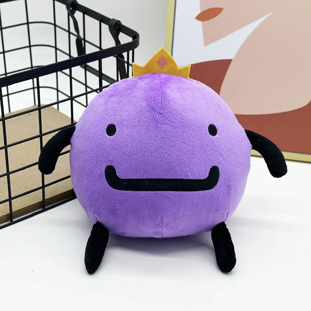 A cute purple plush doll with a yellow crown and black features sitting on a white surface.
