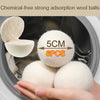 A hand holds several white wool dryer balls inside a washing machine drum.