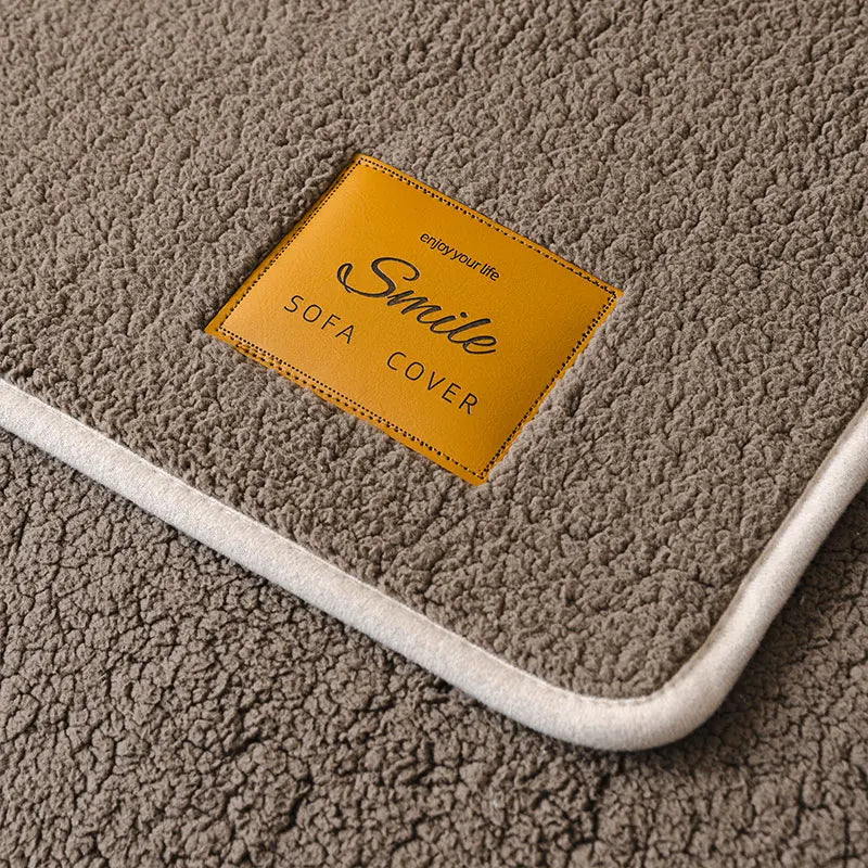 A yellow tag labeled Smile Sofa Cover is placed on a gray, fluffy anti-slip lamb fleece sofa mat.