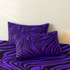 A set of three bold zebra print pillow covers in purple and black on a bed.