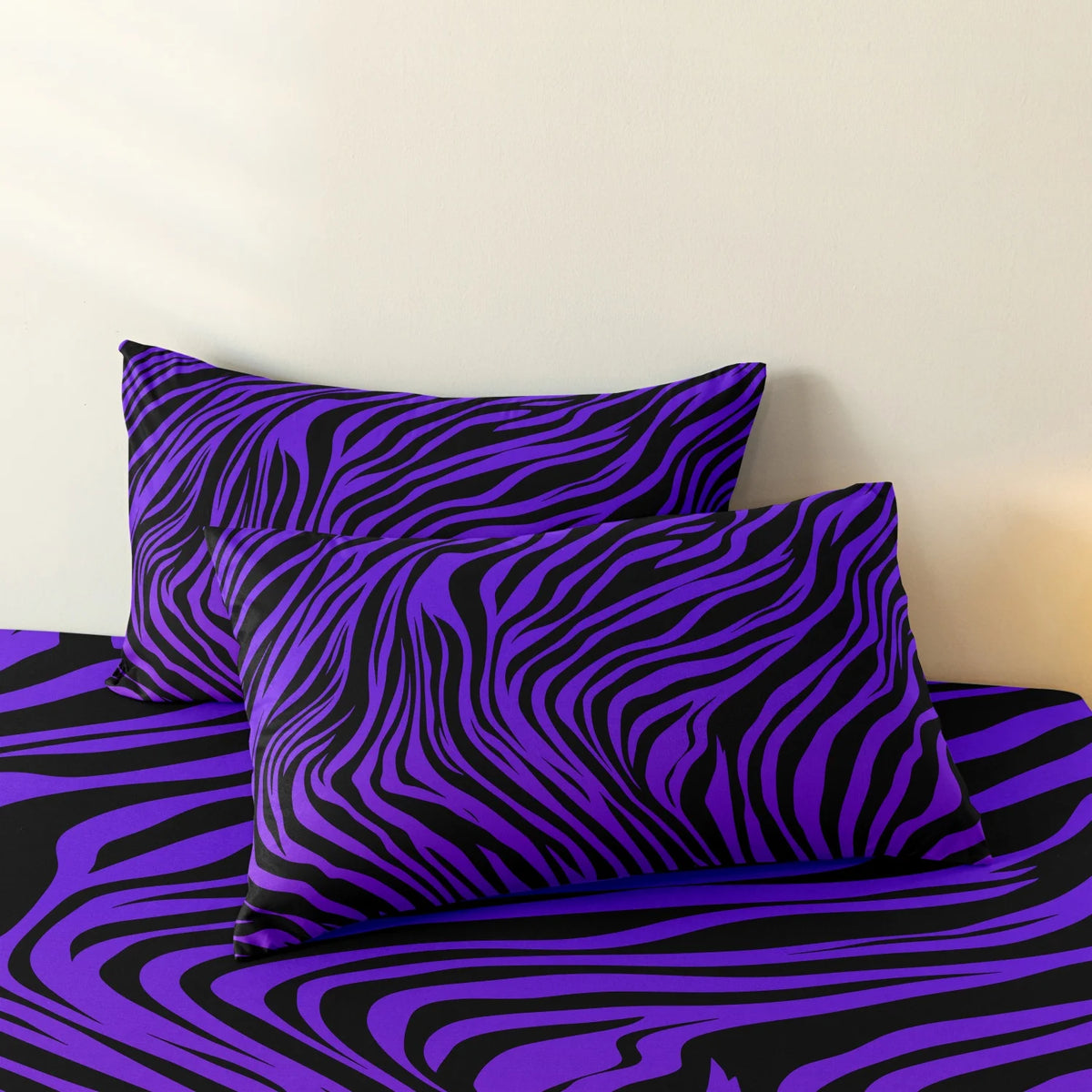A set of three bold zebra print pillow covers in purple and black on a bed.