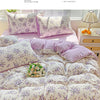 A set of floral duvet cover, flat sheet, and pillowcases in lavender and white floral patterns displayed on a bed.