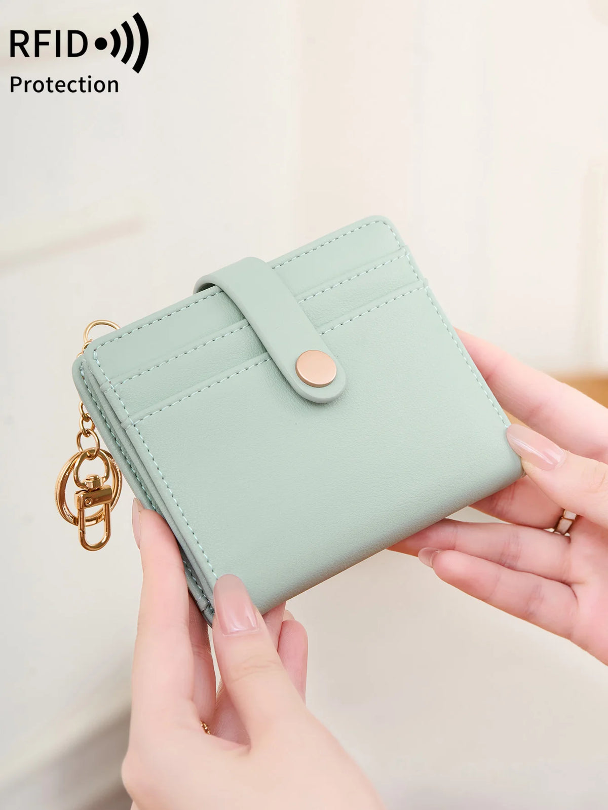 A light mint green bi-fold credit card wallet with a gold chain attached, being held by a person.