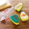 A clear plastic dish wand with a yellow sponge head and a green cleaning pad is shown on a wooden surface.